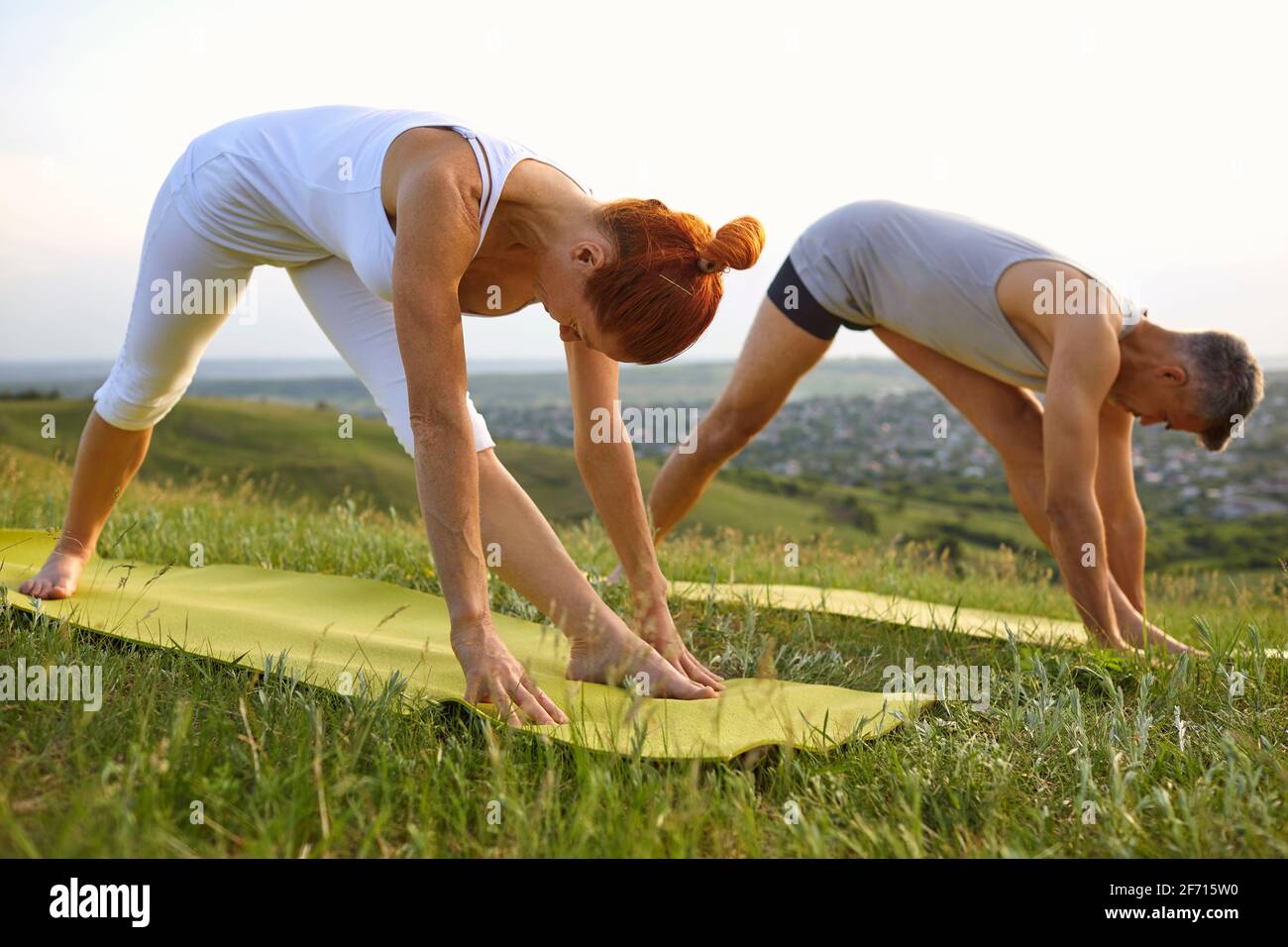 Fit man and woman in fitness clothes doing Parsvottanasana while practicing yoga together in nature in summer Stock Photo