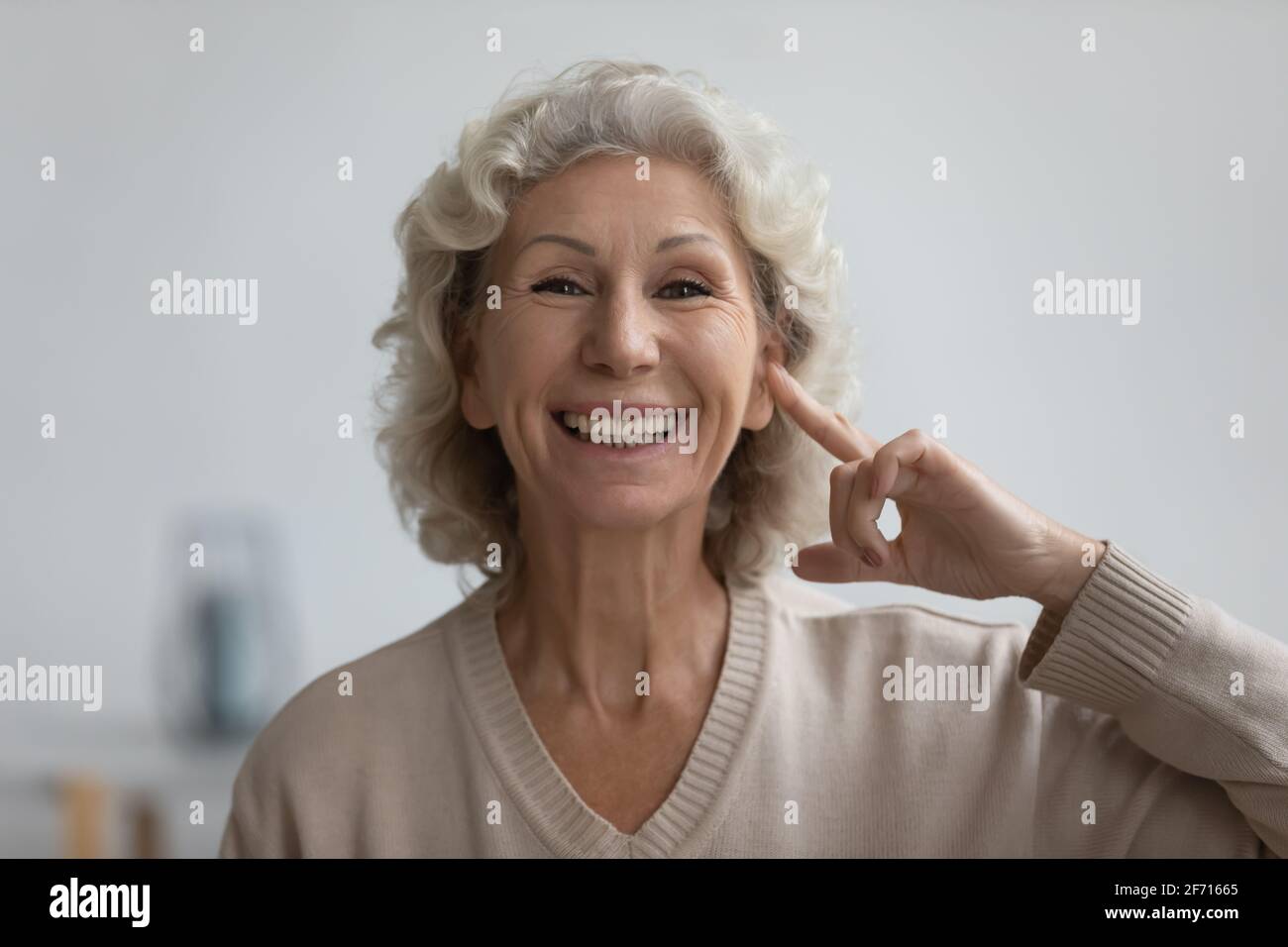 Portrait of happy senior woman pointing finger at her ear Stock Photo