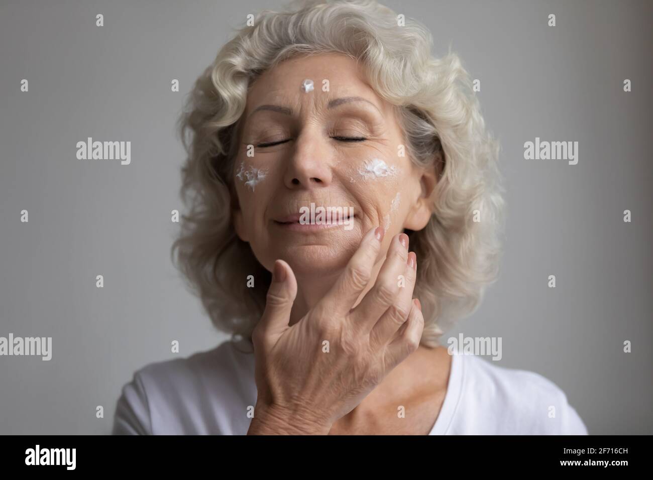 Relaxed elderly woman with closed eyes taking skincare treatment Stock Photo