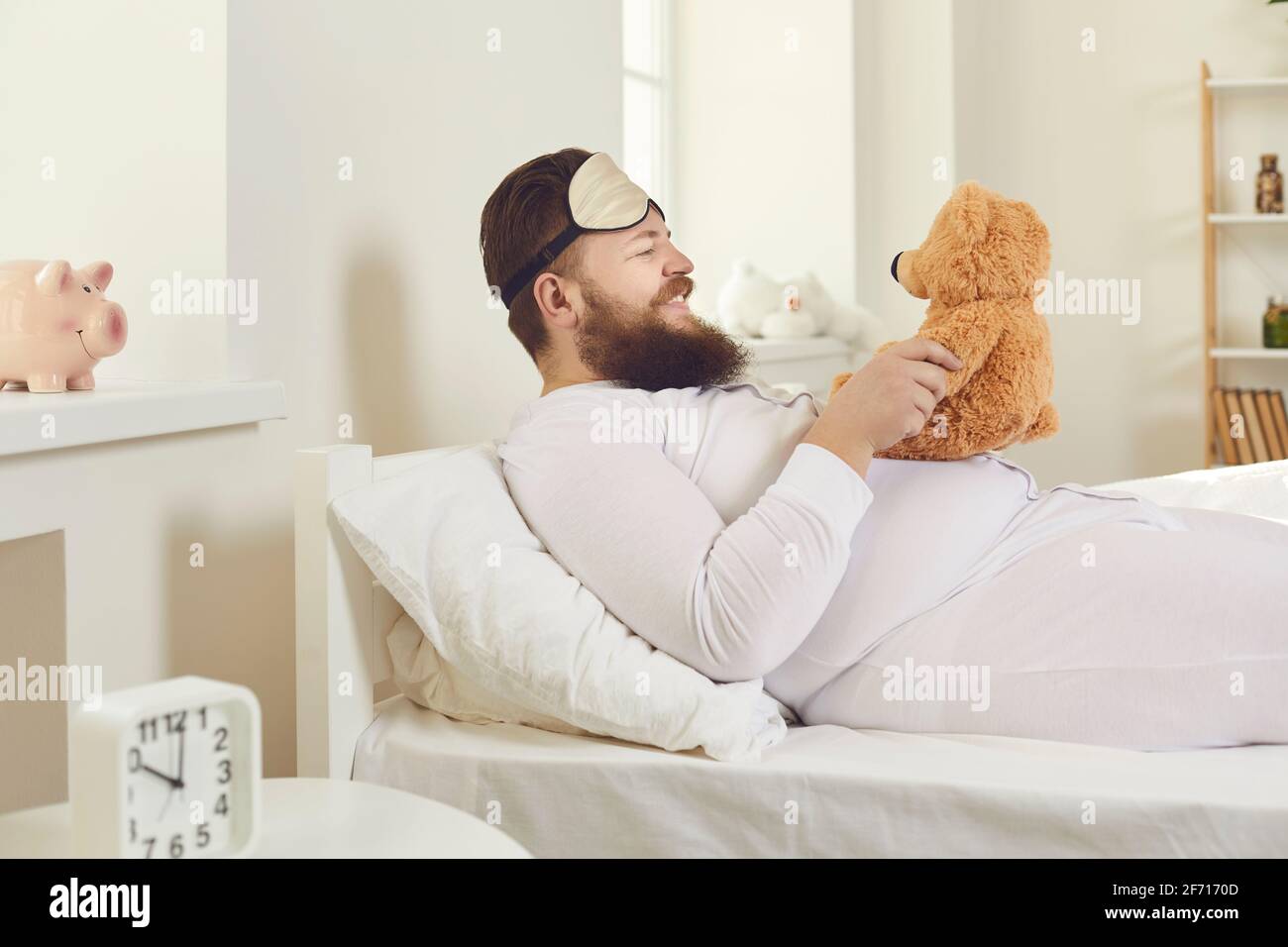 Cheerful man in white pajamas and a sleeping mask woke up and behaves like a child. Stock Photo