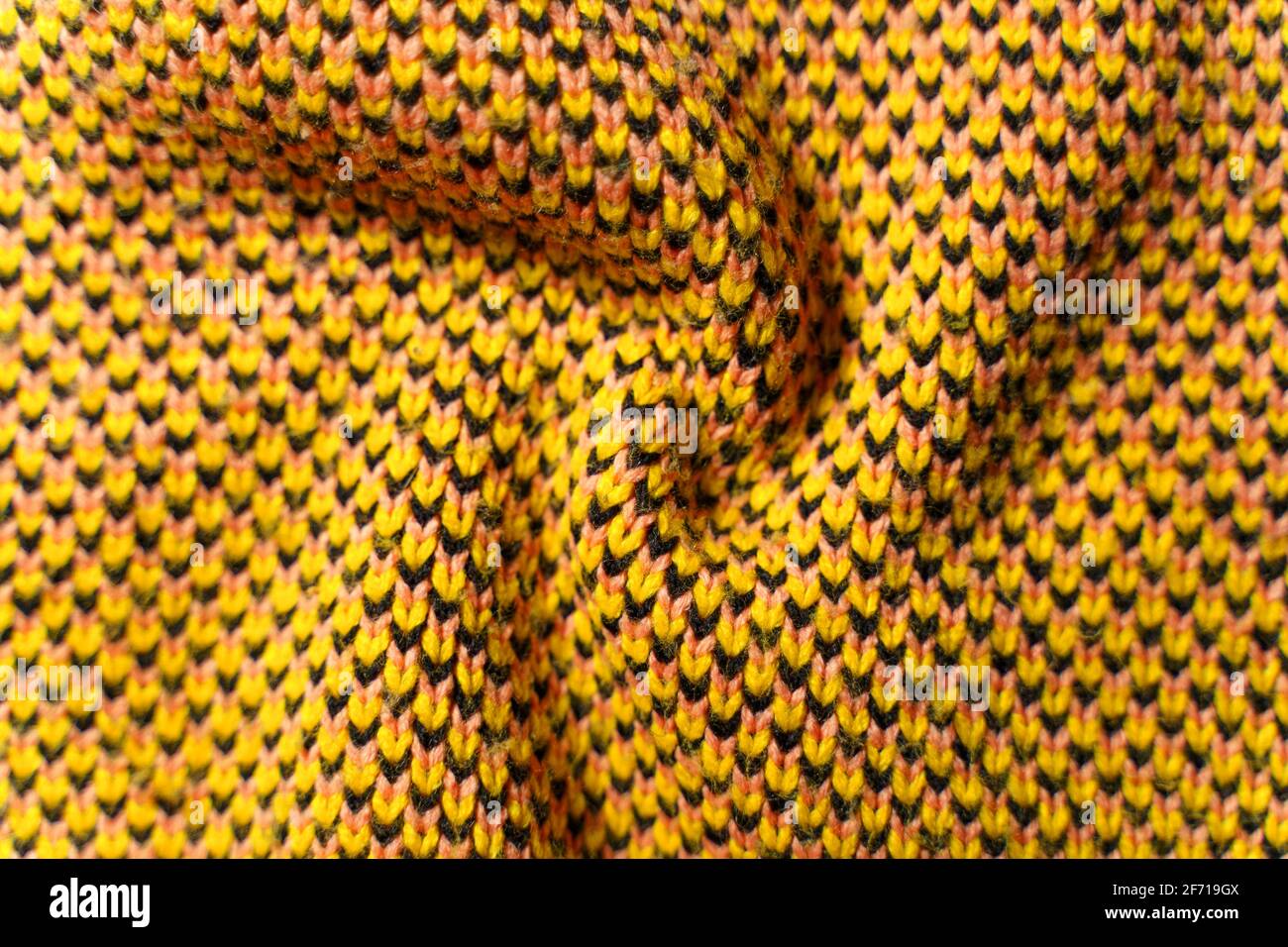 Twisted folds of synthetic knitted fabric with pattern elements of yellow, black and white yarns close up. Multicolor patterned knitted fabric texture Stock Photo