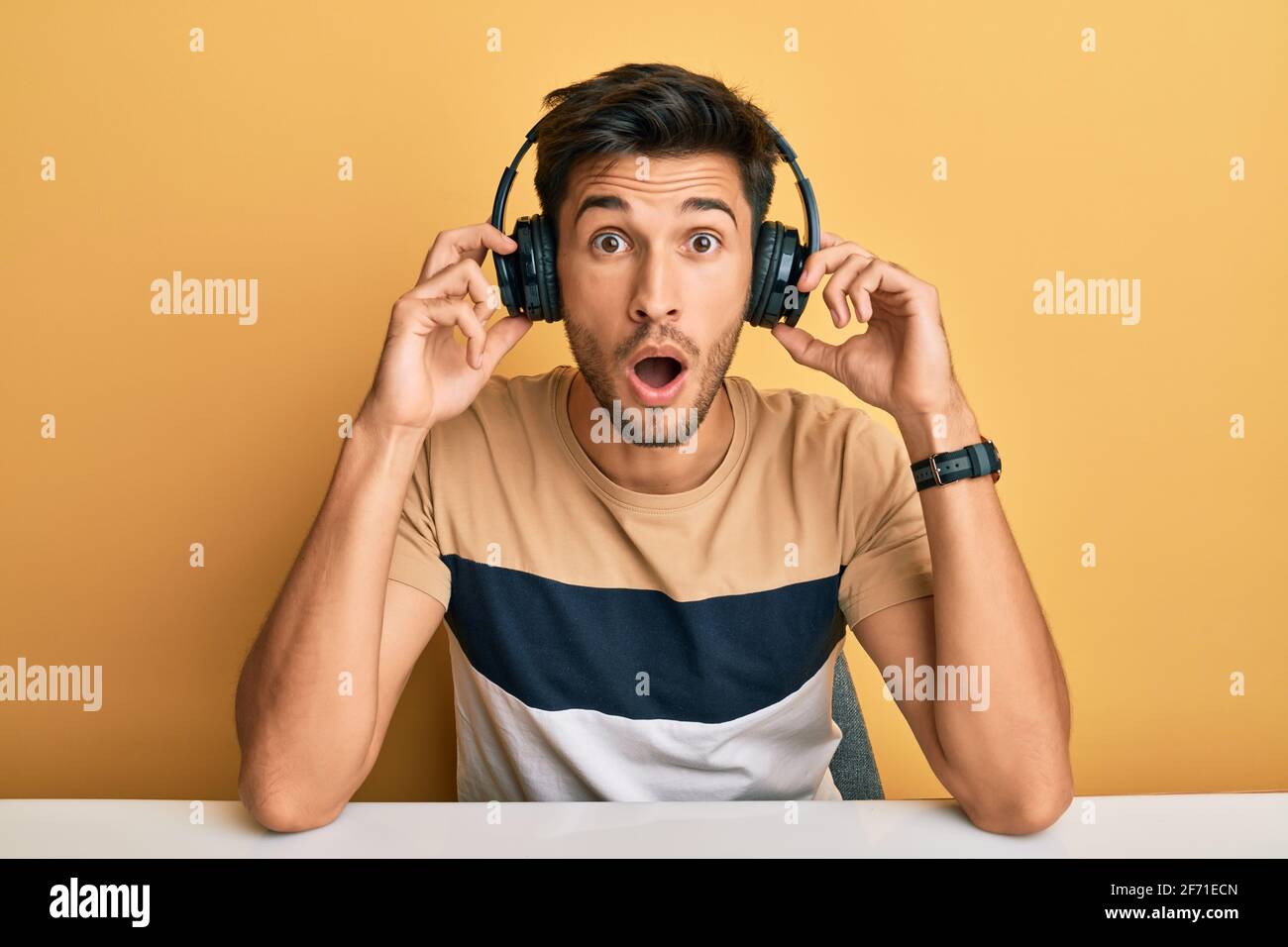 Young handsome man listening to music wearing headphones afraid and shocked with surprise and amazed expression, fear and excited face. Stock Photo