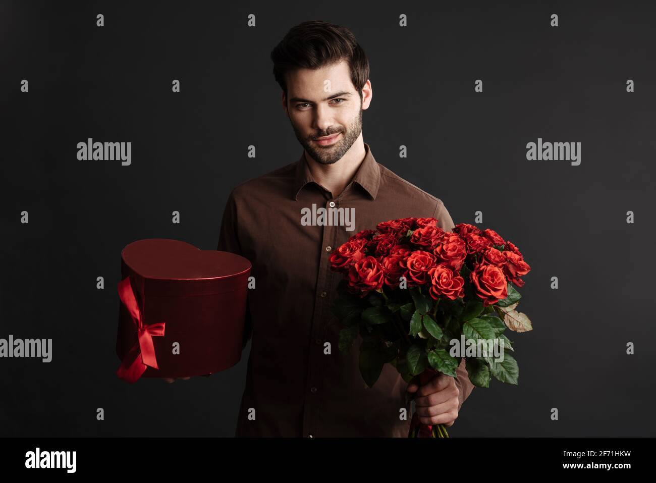 Pleased handsome guy posing with gift box and bouquet of roses isolated ...