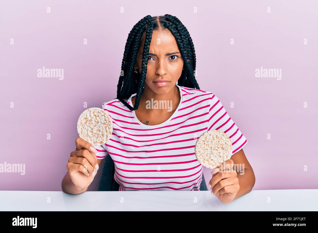 Beautiful hispanic woman eating healthy rice crackers skeptic and