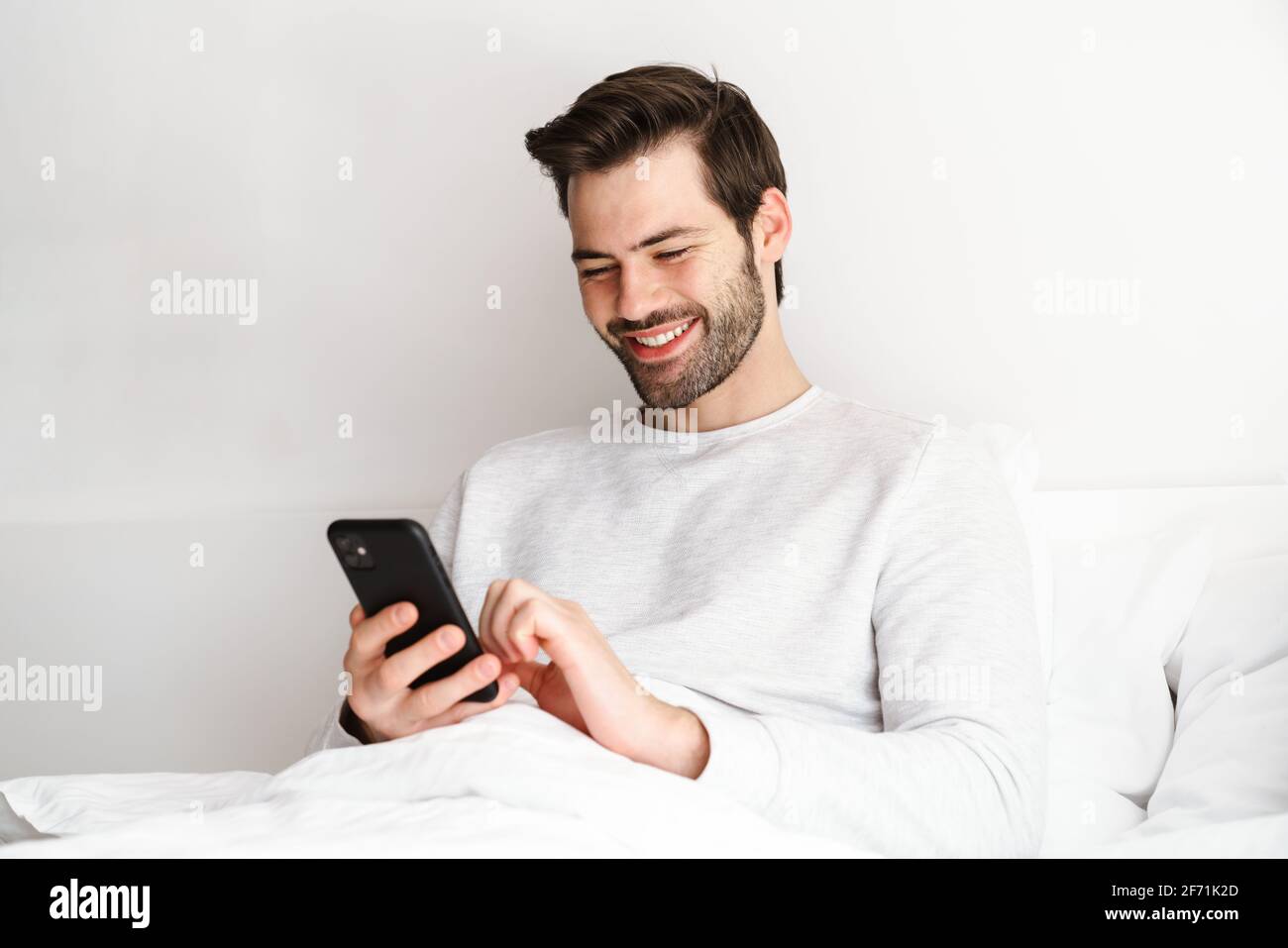 Smiling young man using mobile phone while resting in bed at home Stock Photo