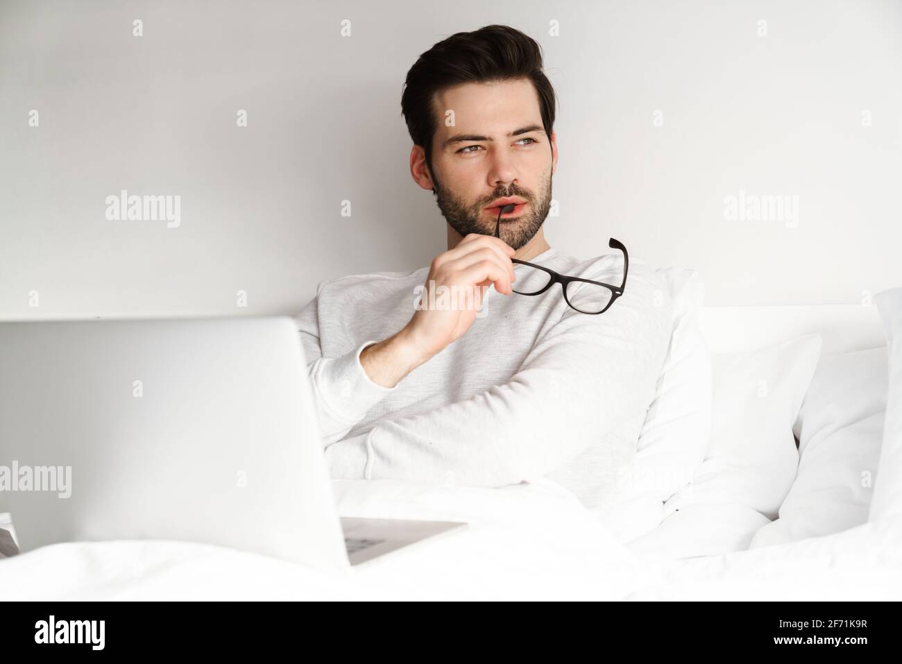 Focused handsome man using laptop while resting in bed at home Stock Photo
