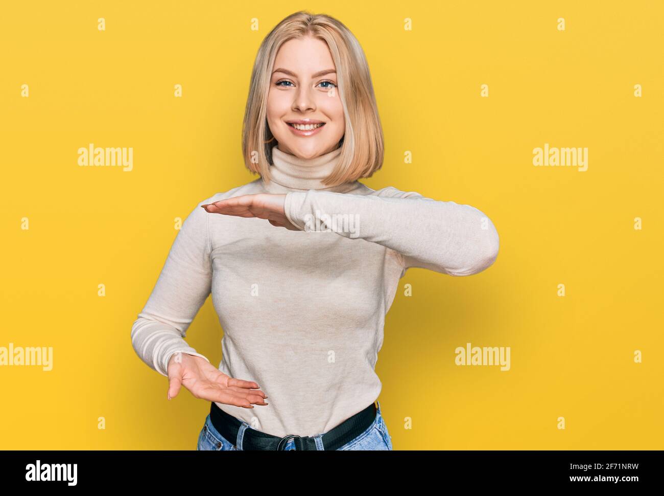 Young blonde woman wearing casual clothes gesturing with hands showing big and large size sign, measure symbol. smiling looking at the camera. measuri Stock Photo