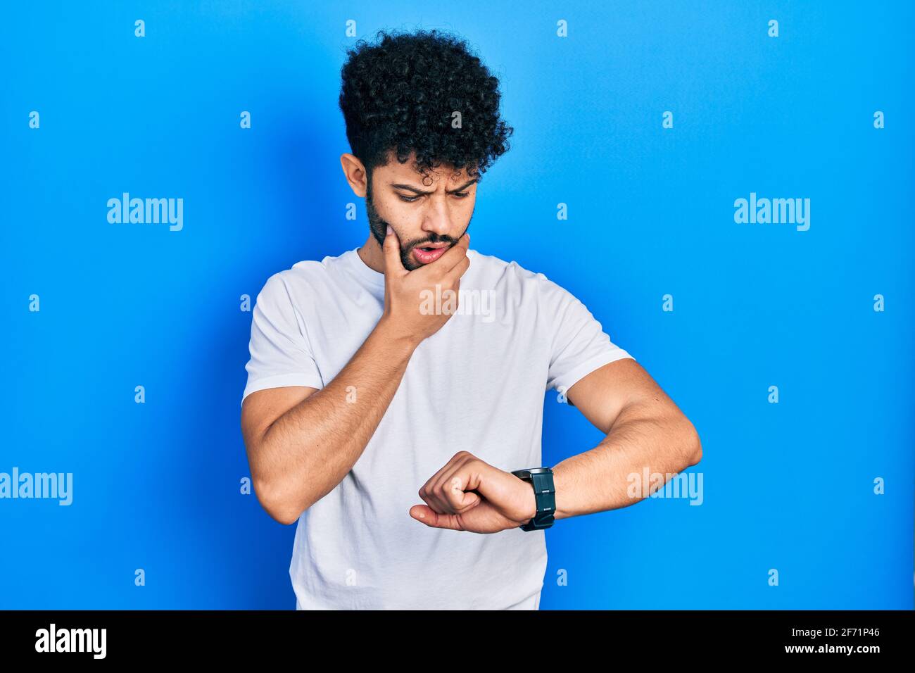 Young arab man with beard wearing casual white t shirt looking at the ...