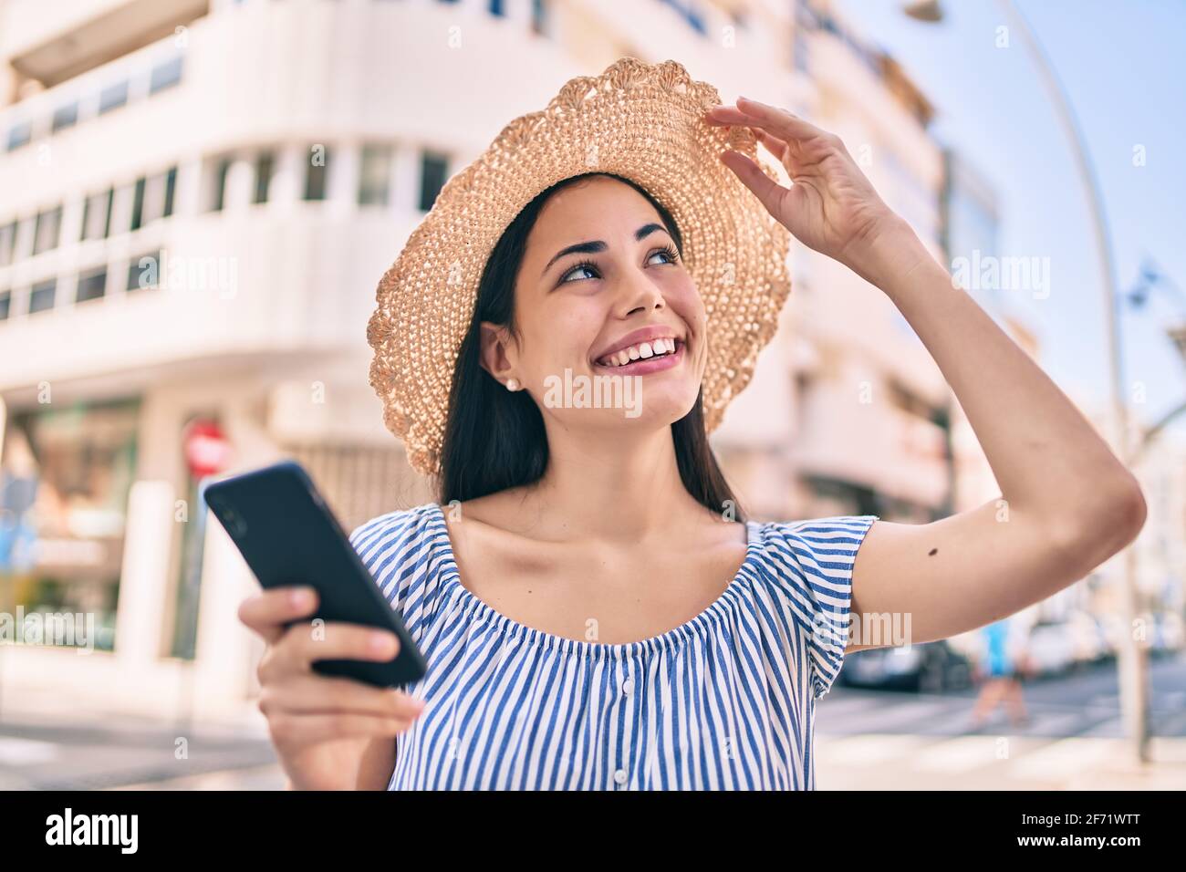 Young latin tourist girl on vacation smiling happy using smartphone at ...
