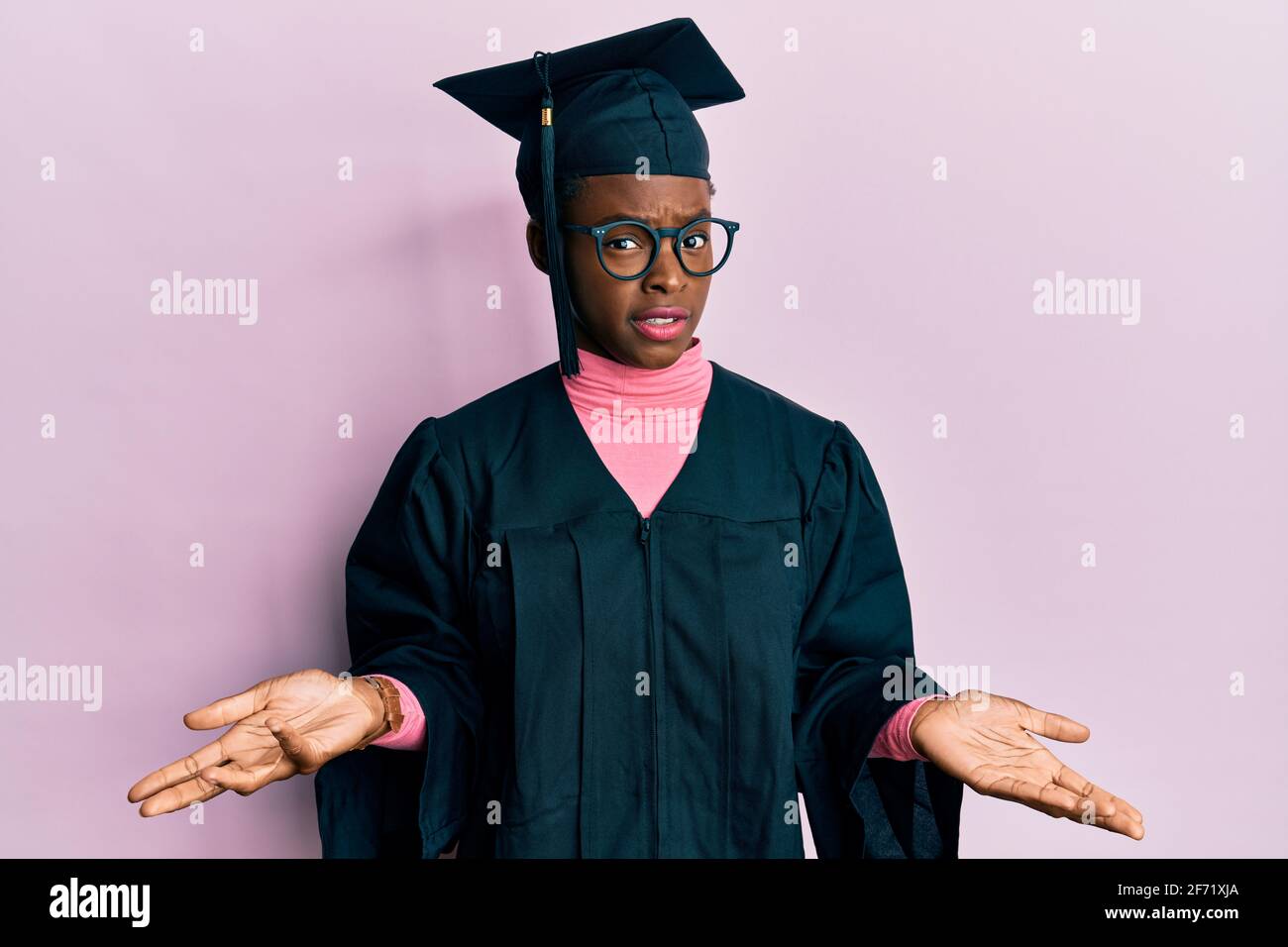 Young african american girl wearing graduation cap and ceremony robe clueless and confused with open arms, no idea concept. Stock Photo