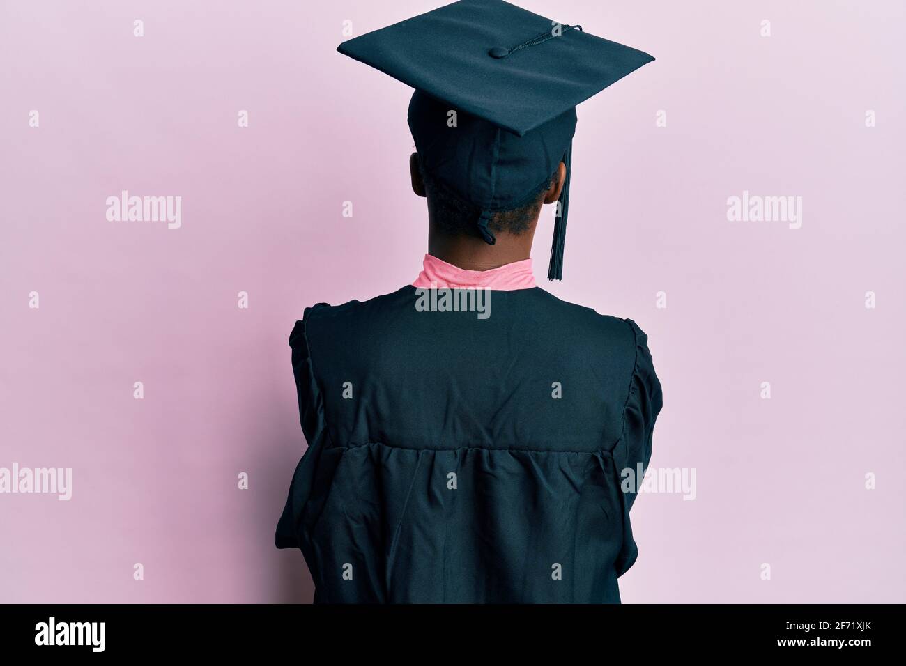 Young african american girl wearing graduation cap and ceremony robe standing backwards looking away with crossed arms Stock Photo
