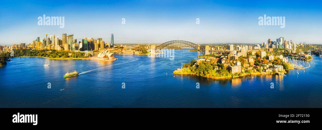 Aerial panorama of City of Sydney over Harbour waters around major CBD landmarks and North Shore connected by the Sydney Harbour bridge. Stock Photo