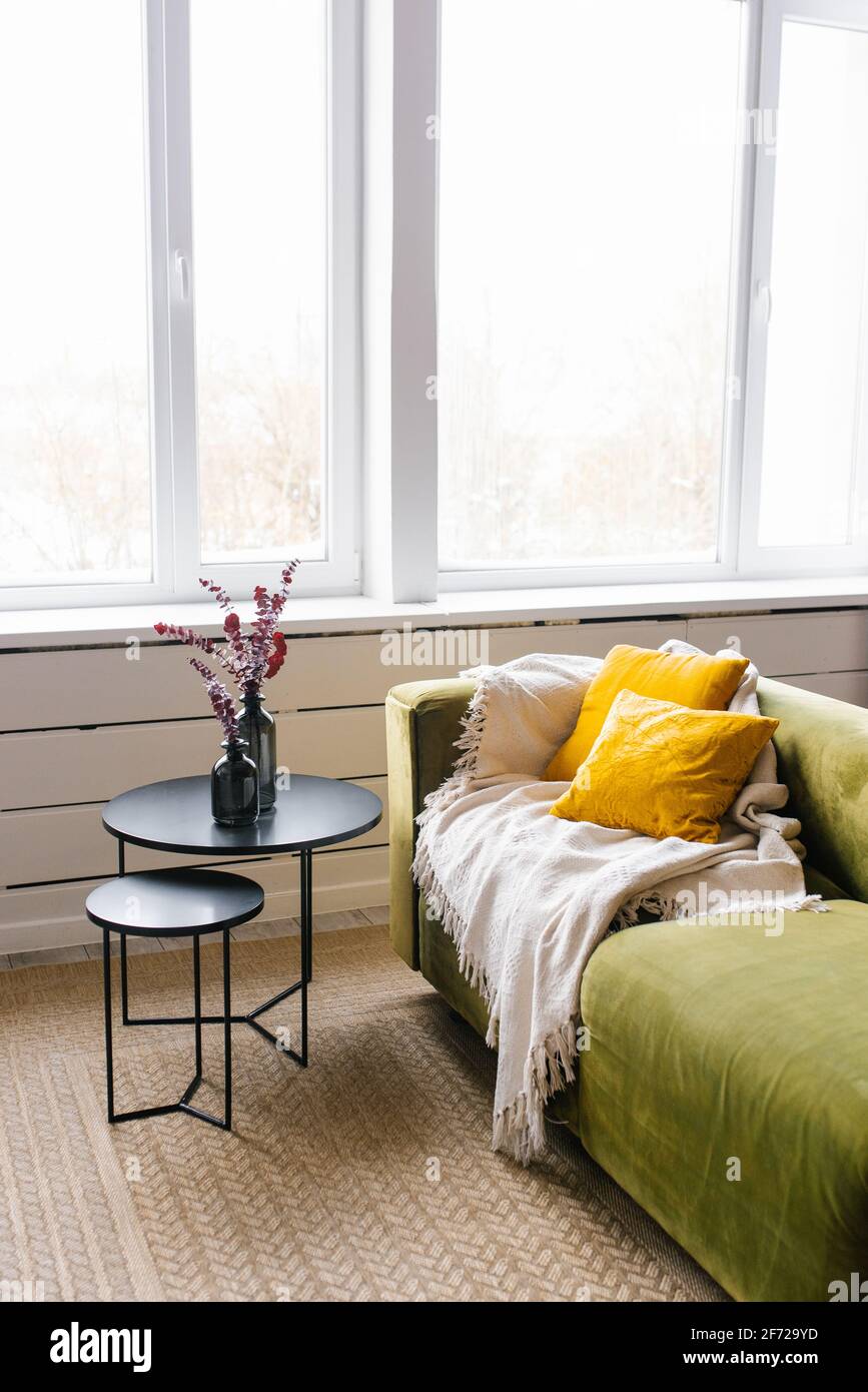 A green sofa with yellow pillows and a beige blanket, a coffee table with a  vase and eucalyptus branches. Modern living room with large window Stock  Photo - Alamy