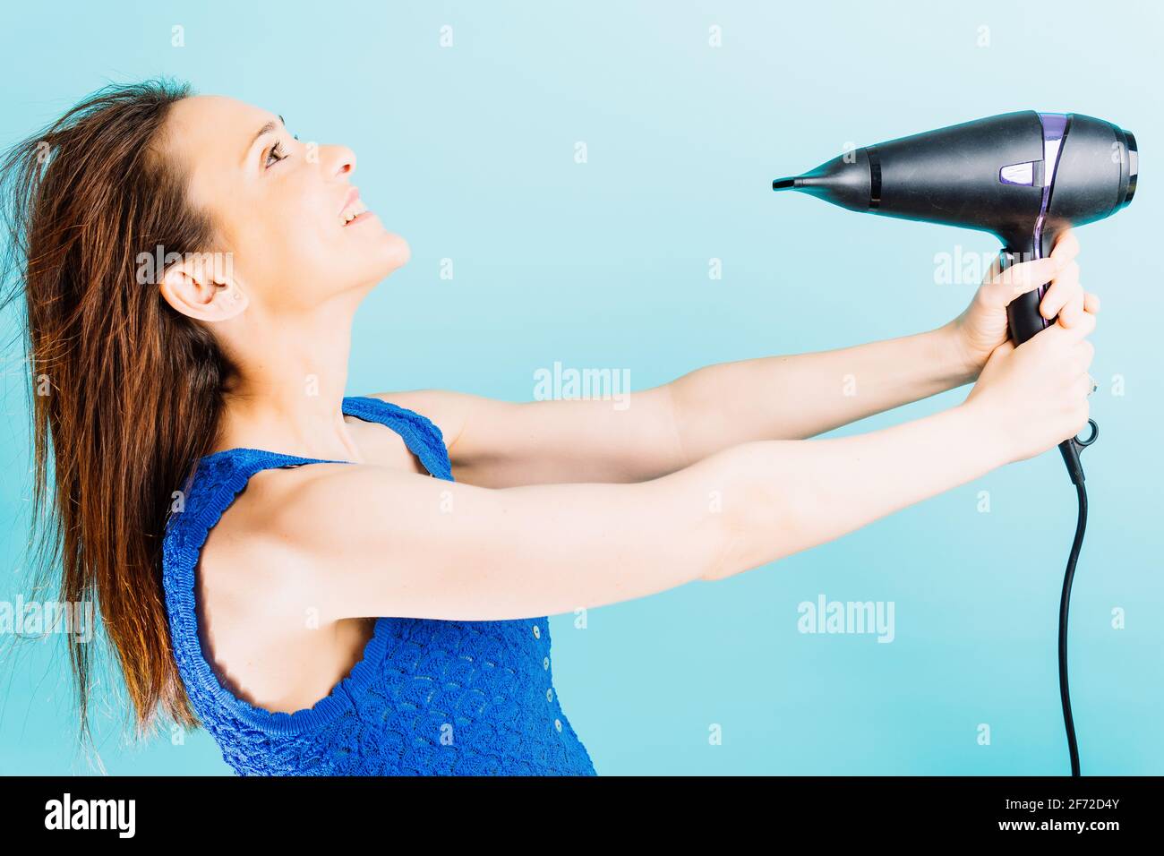 Beautiful young woman drying her hair with blow dryer smiling with blue ...
