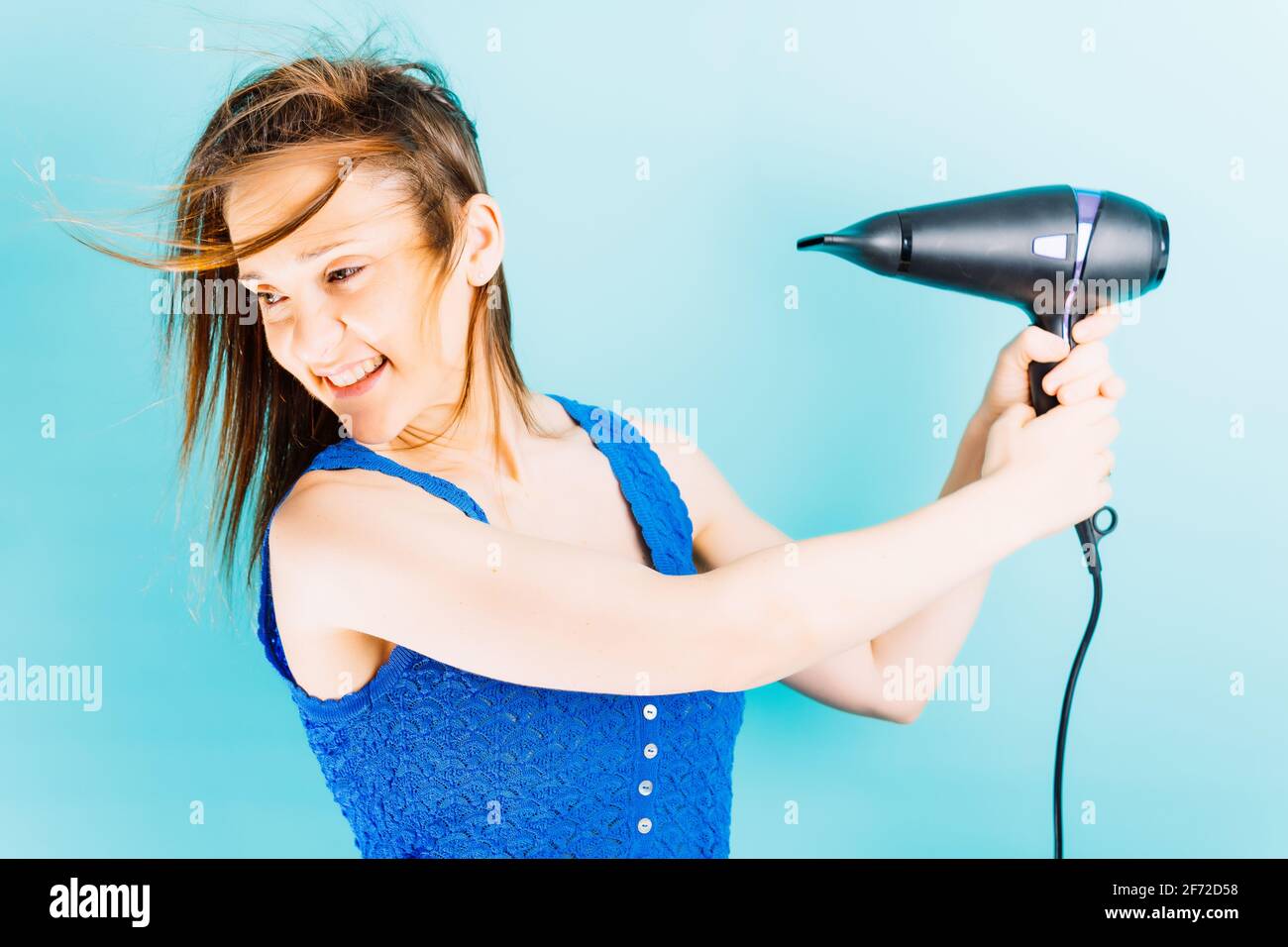 Beautiful young woman drying her hair with blow dryer smiling with blue ...