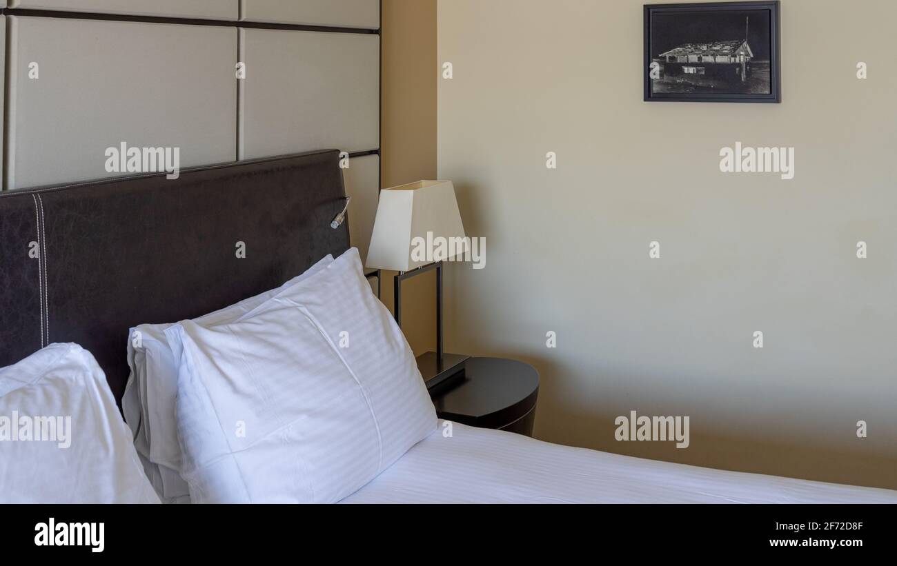 Modern interior hotel bedroom detail. Headboard, pillows, head lamp, artwork on the wall Stock Photo