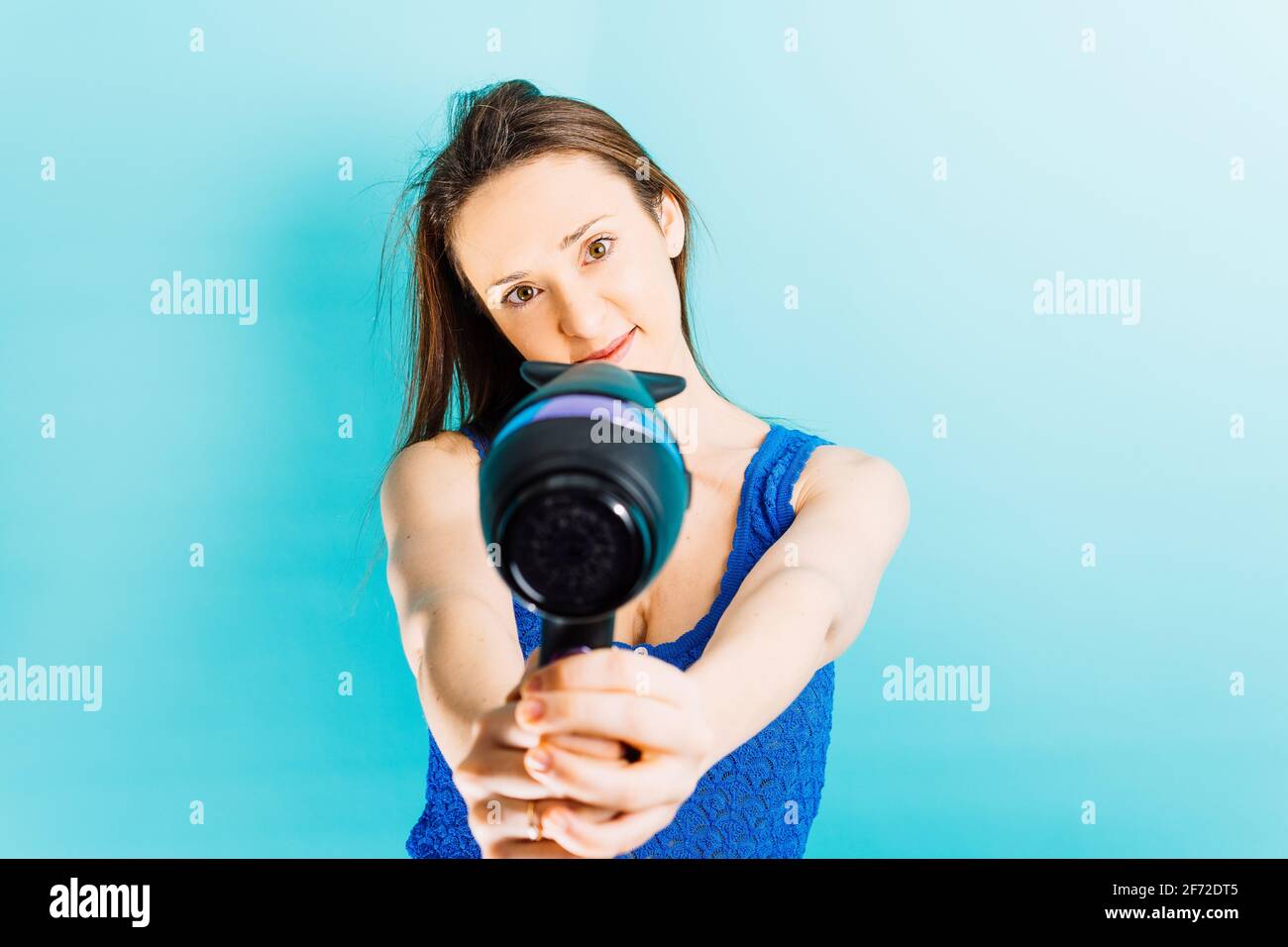 Beautiful young woman drying her hair with blow dryer smiling with blue ...