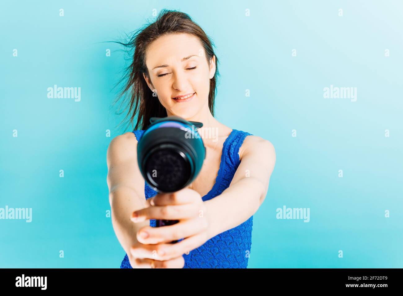 Beautiful young woman drying her hair with blow dryer smiling enjoying ...