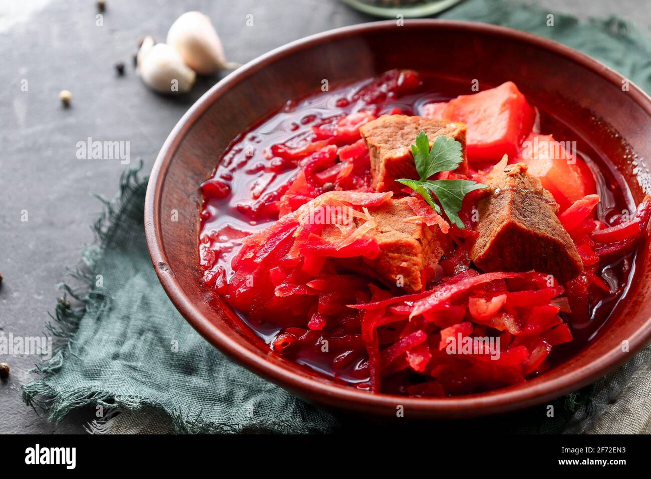 Red borsch with vegetables and meat in a clay plate. Steam from hot tomato soup. Dark background. Delicious healthy lunch. Copy space Stock Photo