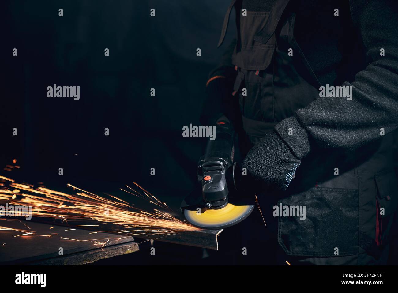 Close up of man in black gloves and special black suit grinding machine working with metal in dark room. Concept of process working with special equipments and with metal. Stock Photo