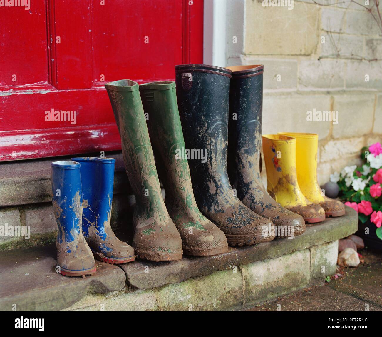 A family of wellington boots left on a doorstep with a red door behind. Stock Photo