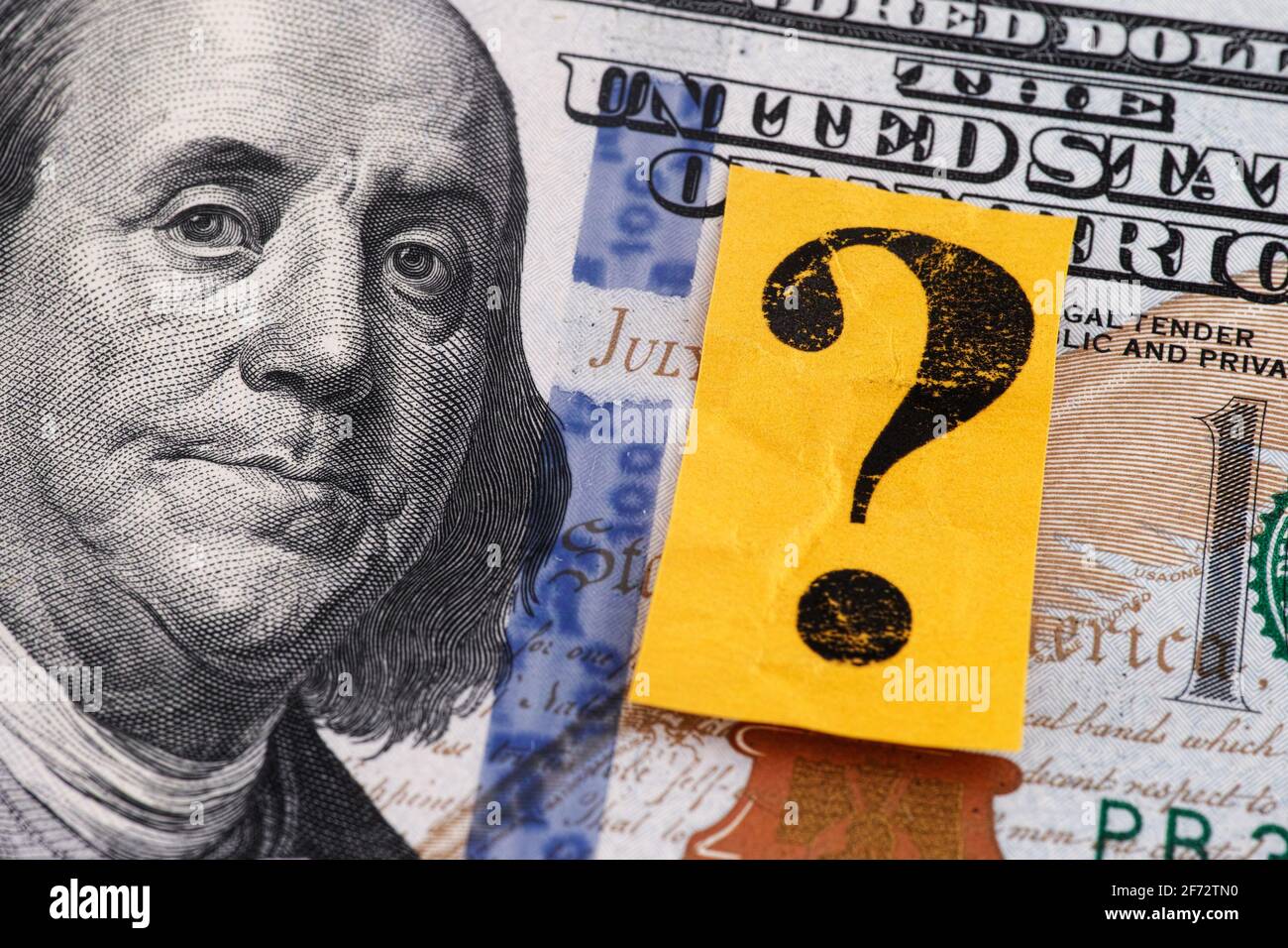 A one hundred dollar bill and a yellow paper note with a question mark on it. Closeup. Stock Photo