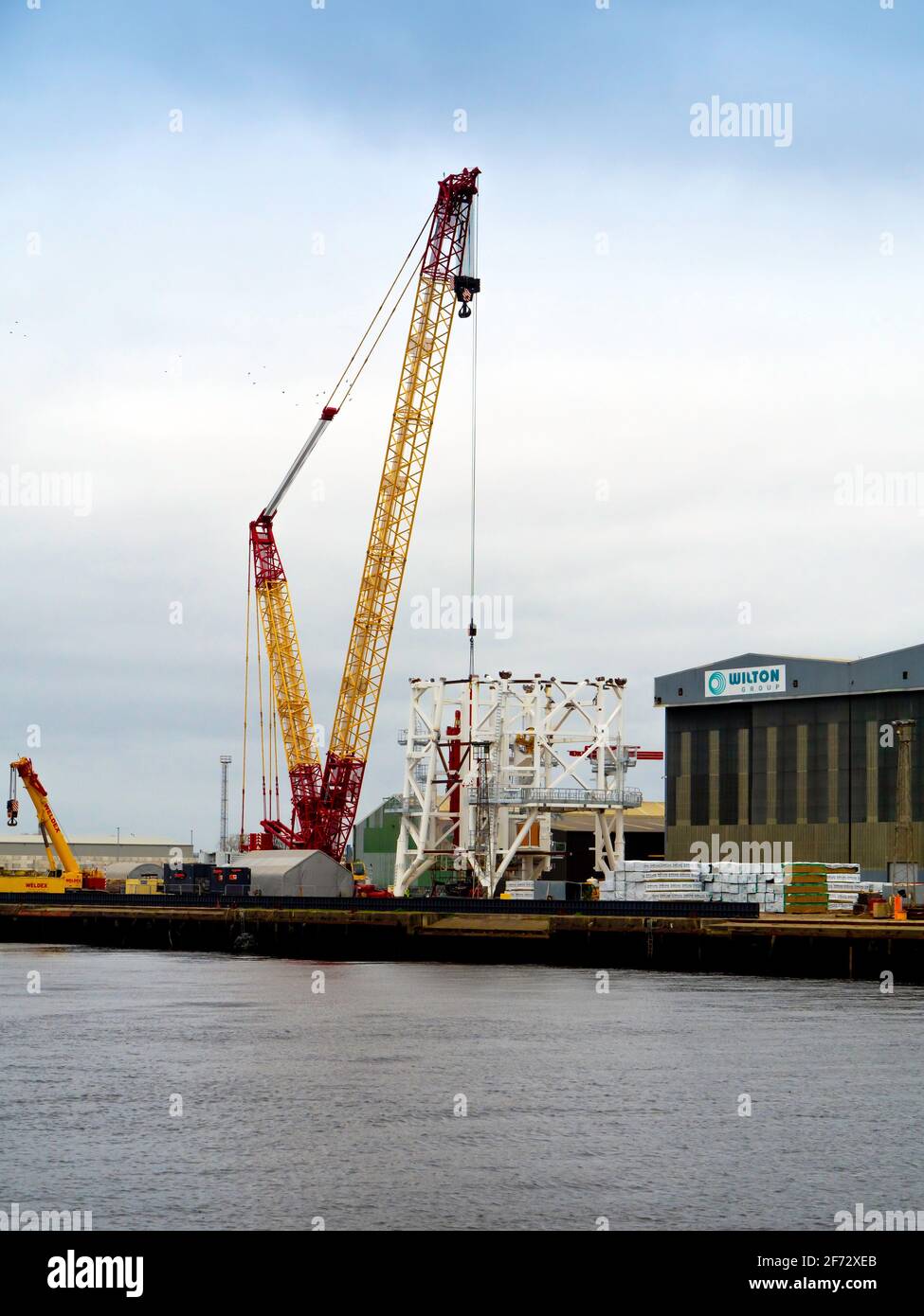 Large mobile crane on the quayside at Wilton Group fabrication yard with a white painted underwater structure at  Port Clarnce on the River Tees Stock Photo