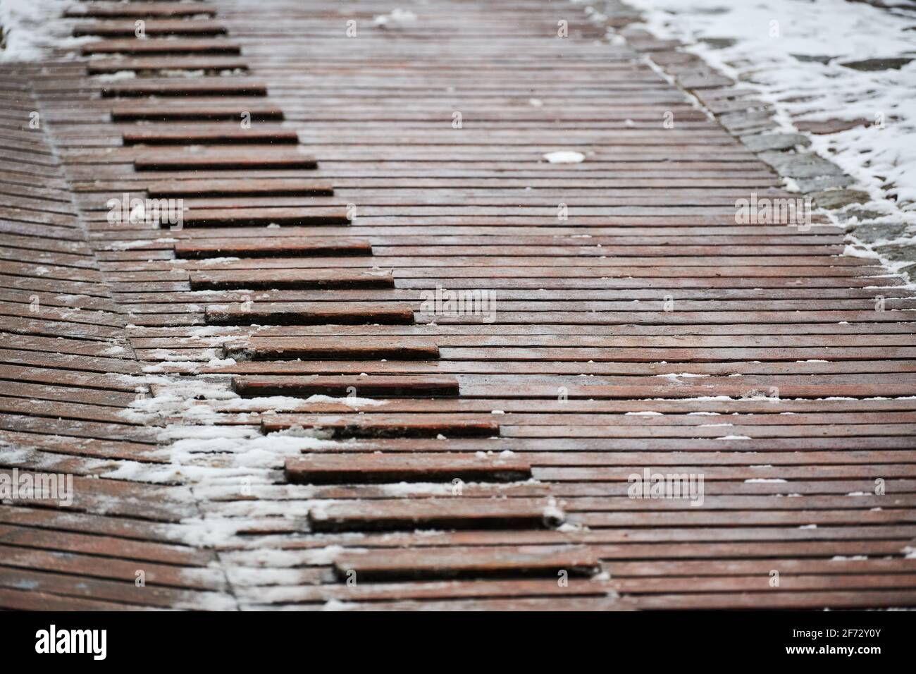 Exterior wooden decking covered with snow. Wooden ramp on playground with non-slip crossbeams, used to ascend up inclined plane. Stock Photo