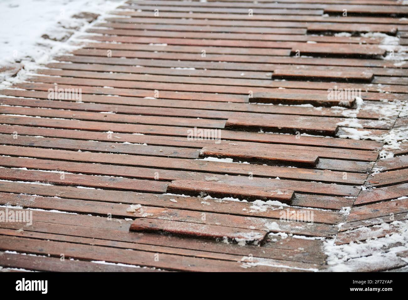 Exterior wooden decking covered with snow. Wooden ramp on playground with non-slip crossbeams, used to ascend up inclined plane. Stock Photo