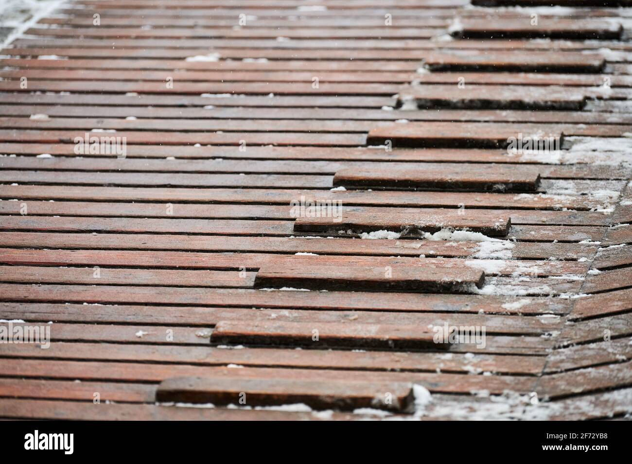 Exterior wooden decking covered with snow. Wooden ramp on playground with non-slip crossbeams, used to ascend up inclined plane. Stock Photo