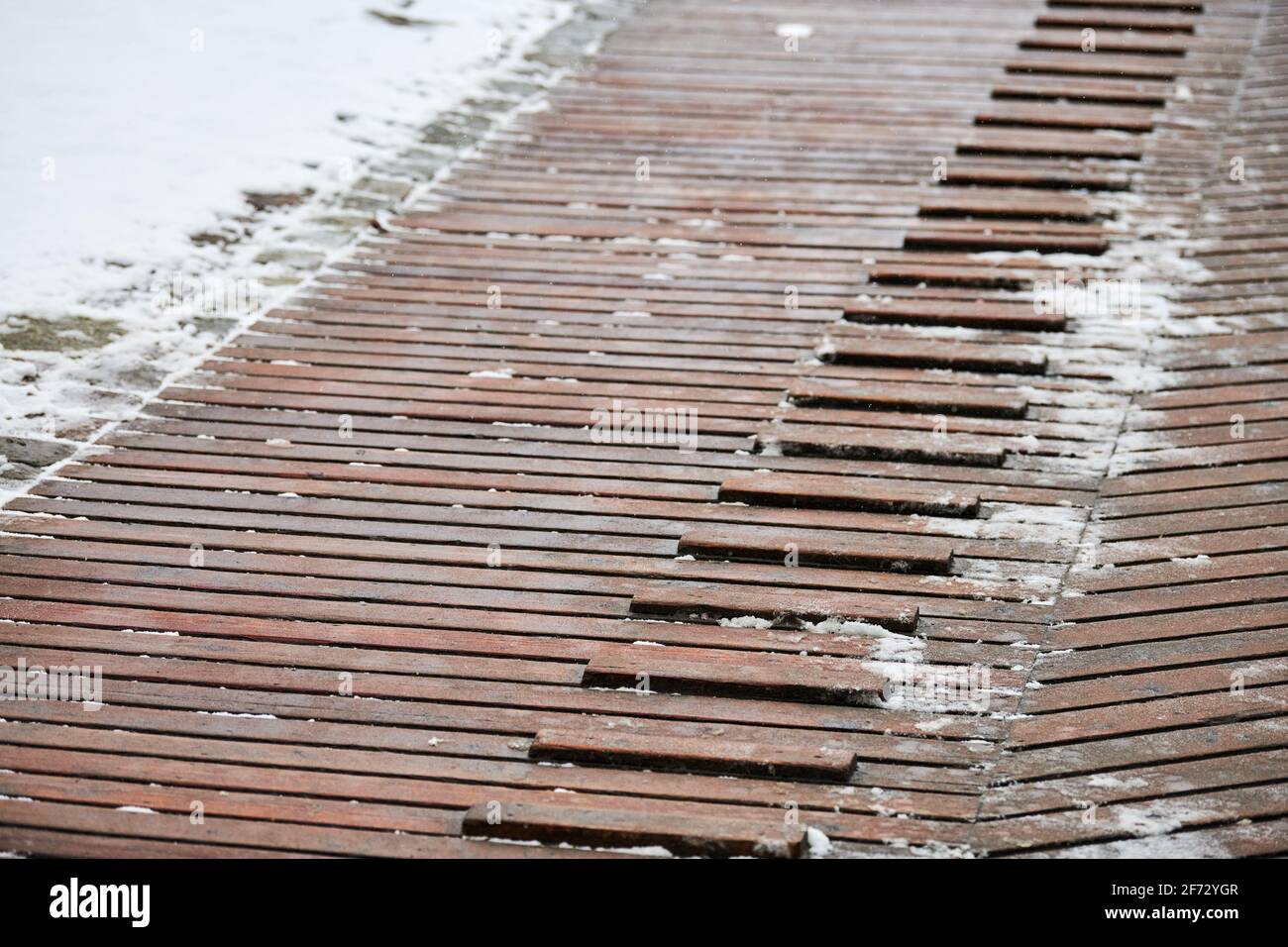 Exterior wooden decking covered with snow. Wooden ramp on playground with non-slip crossbeams, used to ascend up inclined plane. Stock Photo