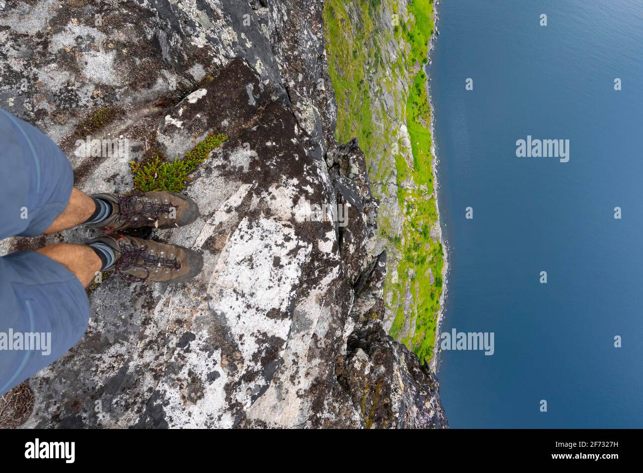 Hiker standing on steep cliff, vertical drop to fjord, Mount Barden, Senja, Norway Stock Photo