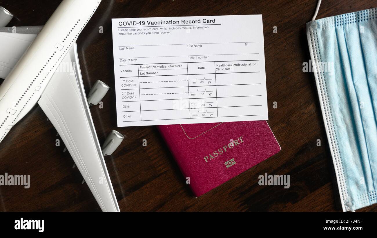 COVID-19 Vaccination Record Card on desk, coronavirus immunization certificate and tourist passport. Top view of paper medical form required for trave Stock Photo
