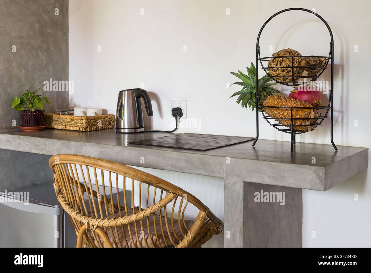 Interior of hotel or home room, Sri Lanka. Small kitchen table with dishes, pineapple, tropical fruits. Mini bar fridge and light wicker chair inside Stock Photo