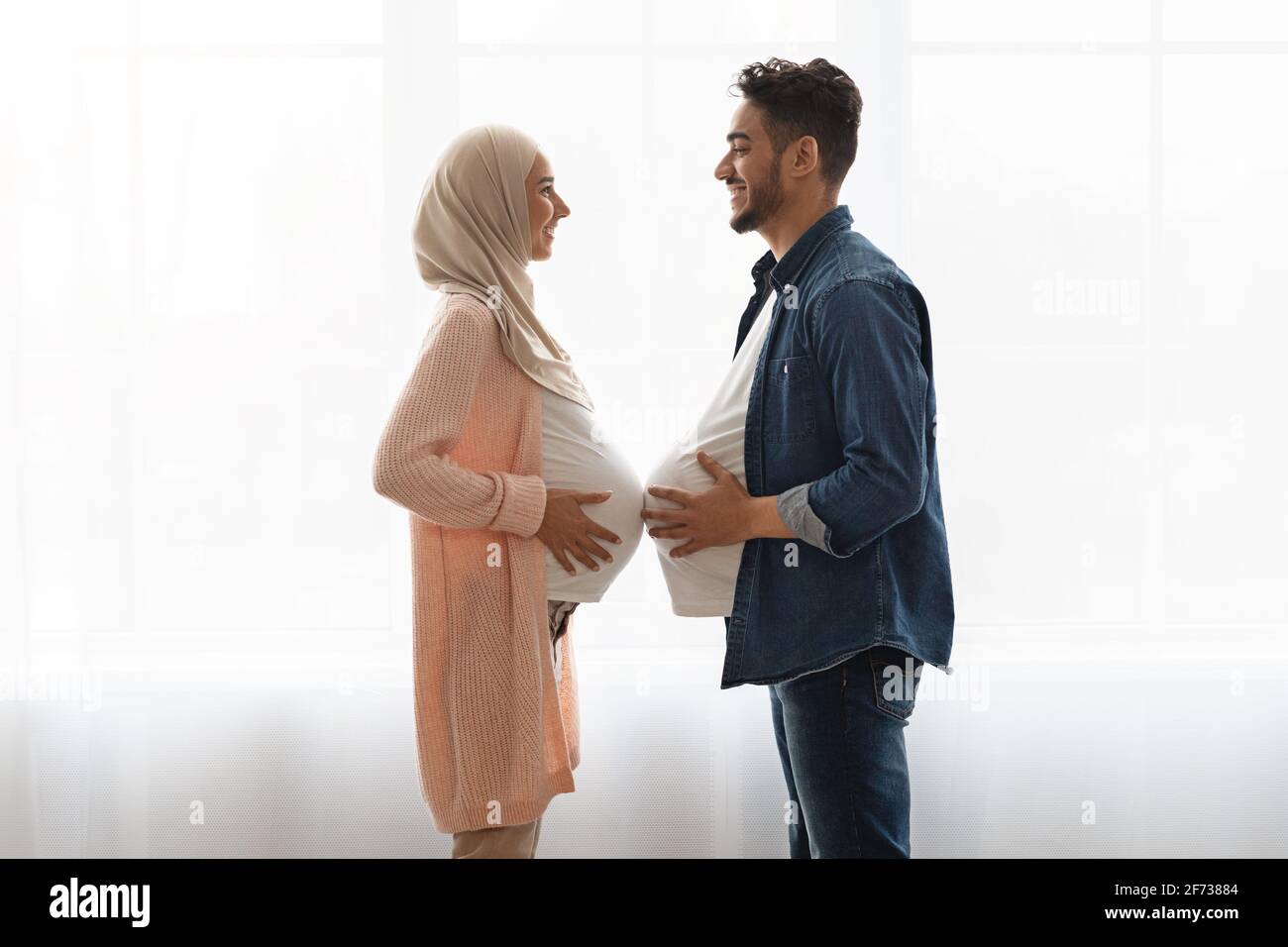 Pregnant islamic lady in hijab comparing belly sizes with her husband