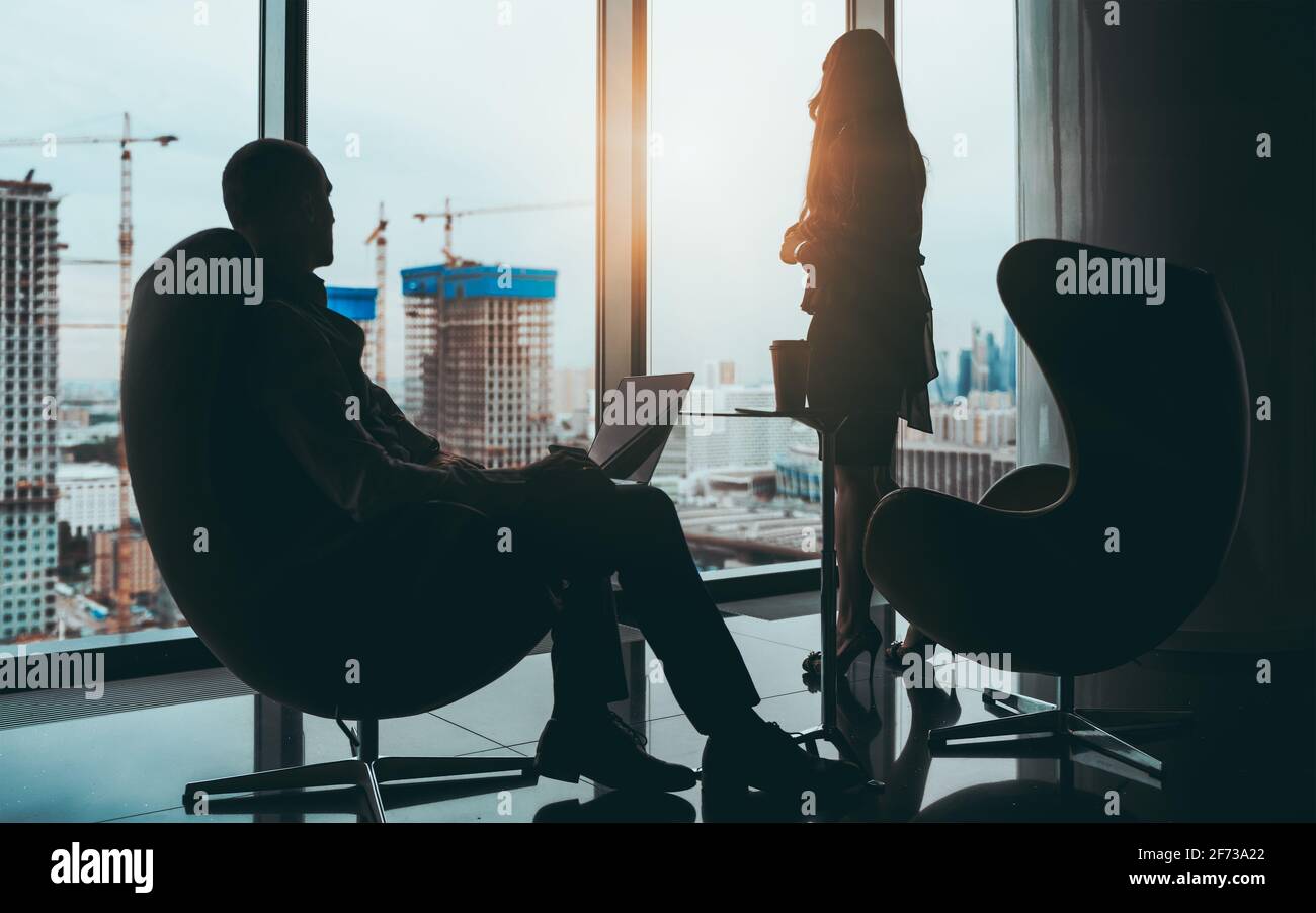 A business scene: silhouettes of two entrepreneurs near a panoramic window of a skyscraper with a construction site outside, selective focus on a busi Stock Photo