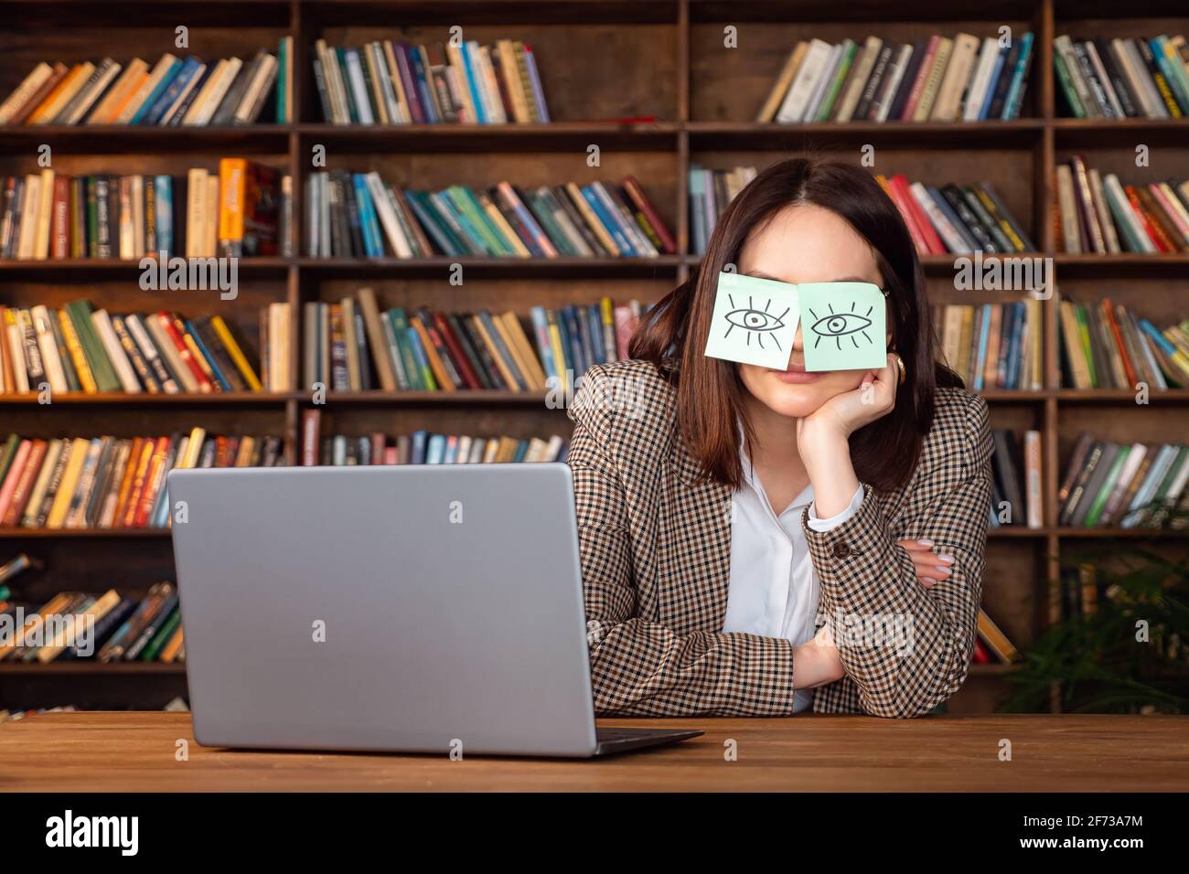 Funny lazy office worker napping at workplace covering eyes with sticky notes. Cheating to sleep concept Stock Photo