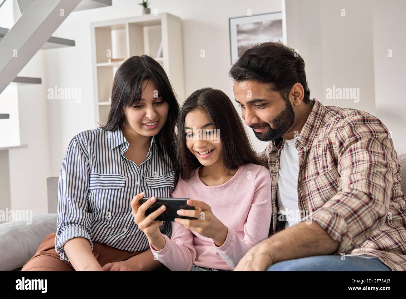 Happy indian family and teen daughter using smart phone at home. Stock Photo