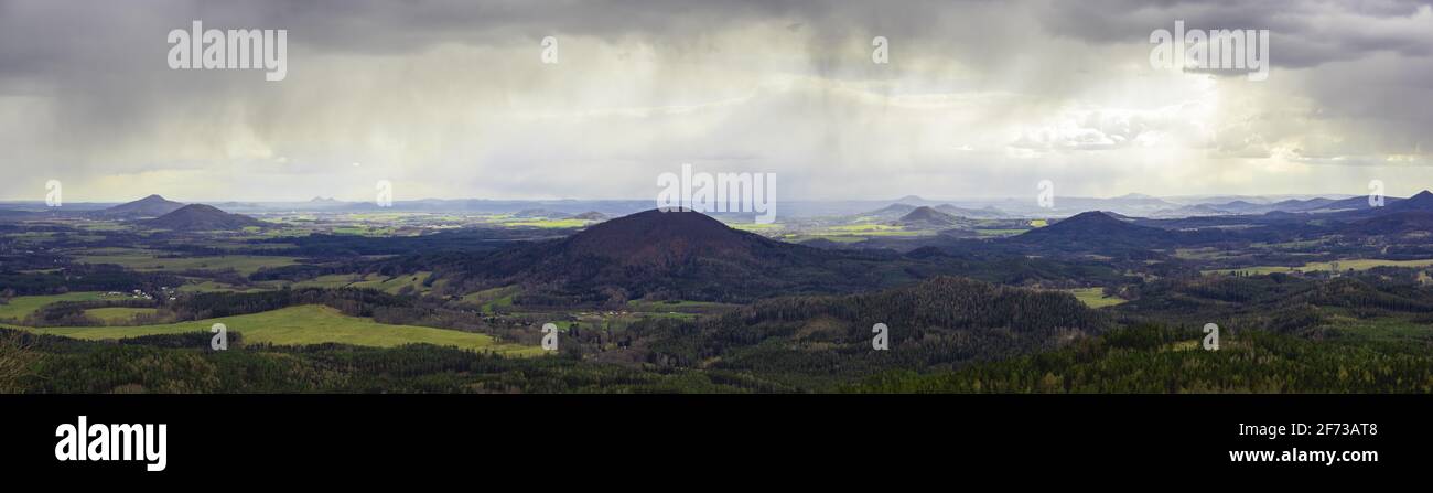 scenic view of rolling hills in the Bohemian Lusatian Mountains with patches of sunlight and storm clouds and rain plumes. Mount Ralsko, Mount Tlustek Stock Photo