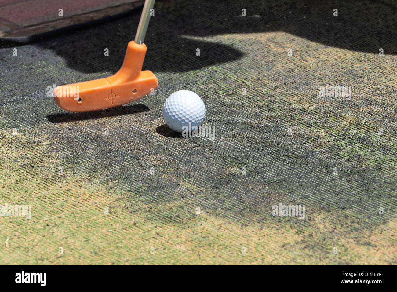 Close up of a minature or mini golf ball and orange putter on artificial grass outdoors with copy space. Stock Photo