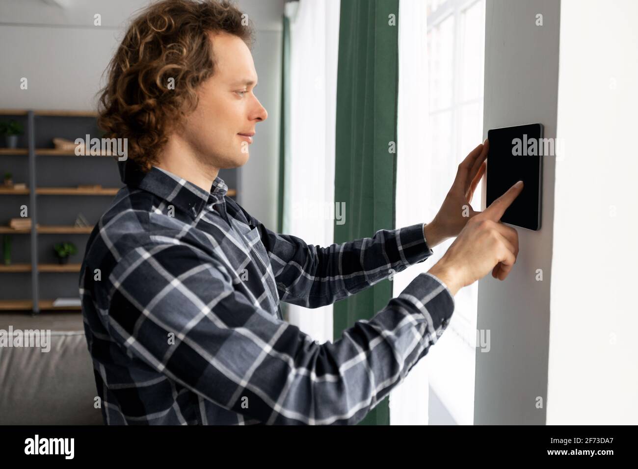 Guy Using Tablet On Wall With Smart Home Application Indoors Stock Photo