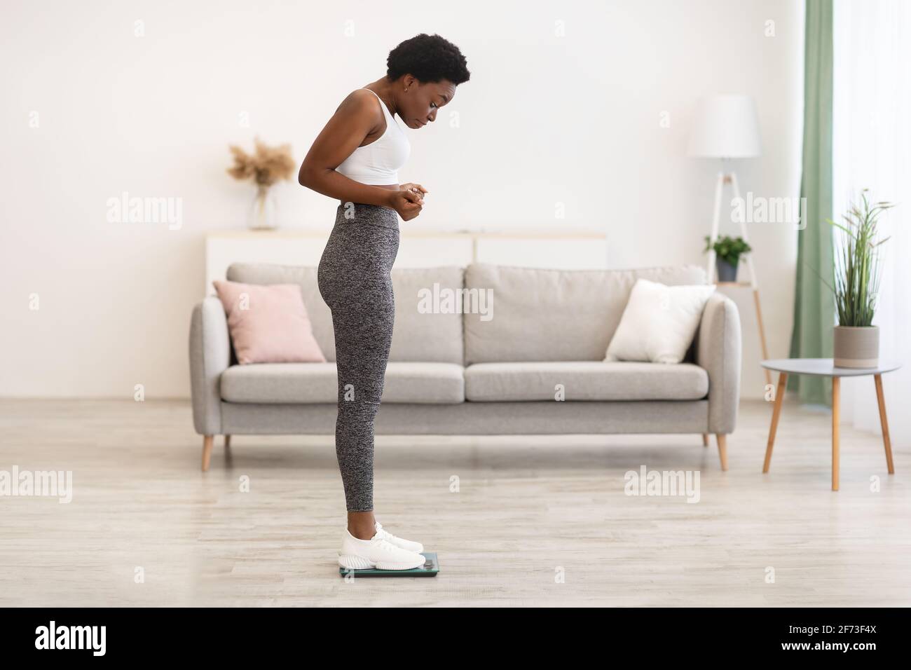 Black Female Standing On Scales Weighing After Weight Gain Indoor Stock Photo