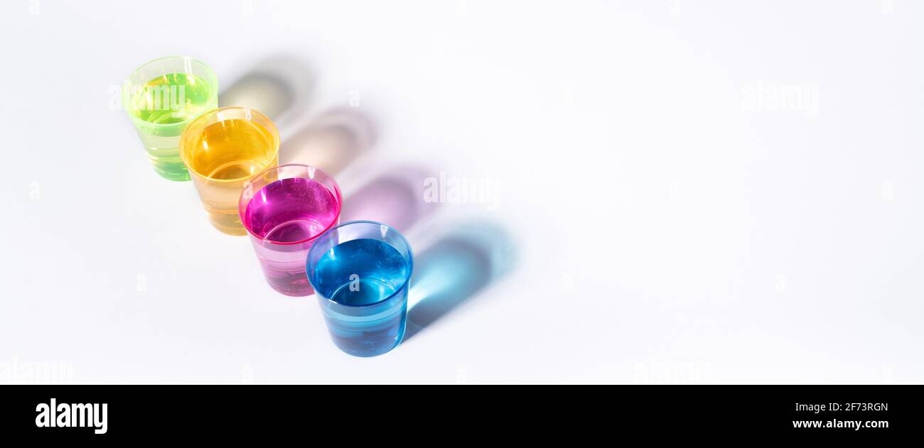 Plastic multi-colored glasses with liquid on a white background with highlights. Layout, mockup. Stock Photo