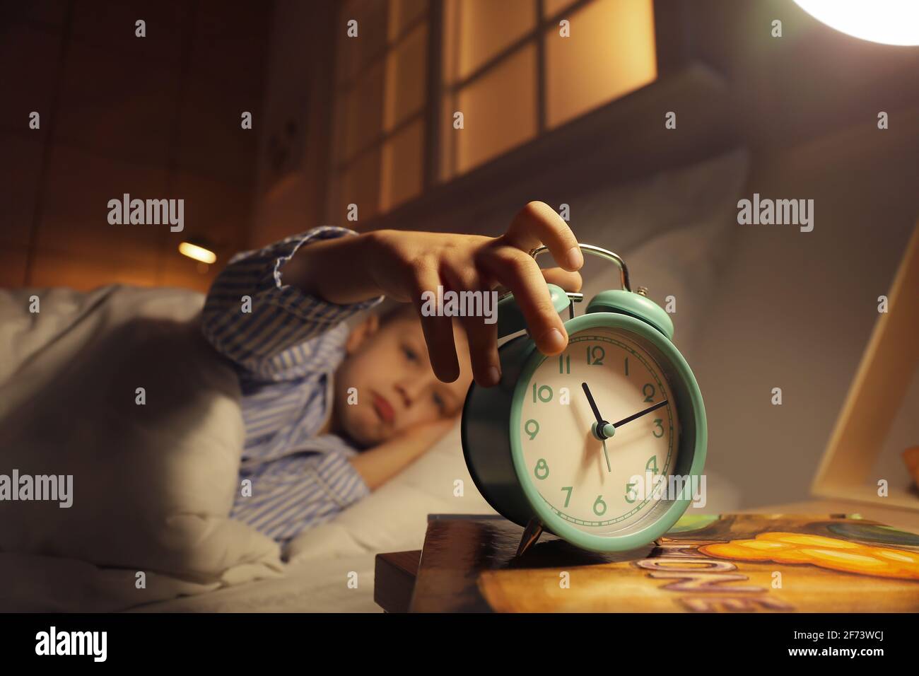 Sleepy little boy turning off alarm clock at night Stock Photo Alamy