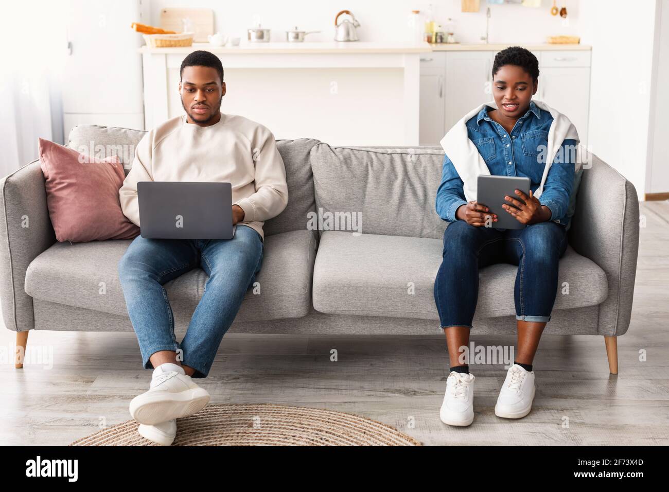 African american couple sitting on couch, using laptop and tablet Stock ...