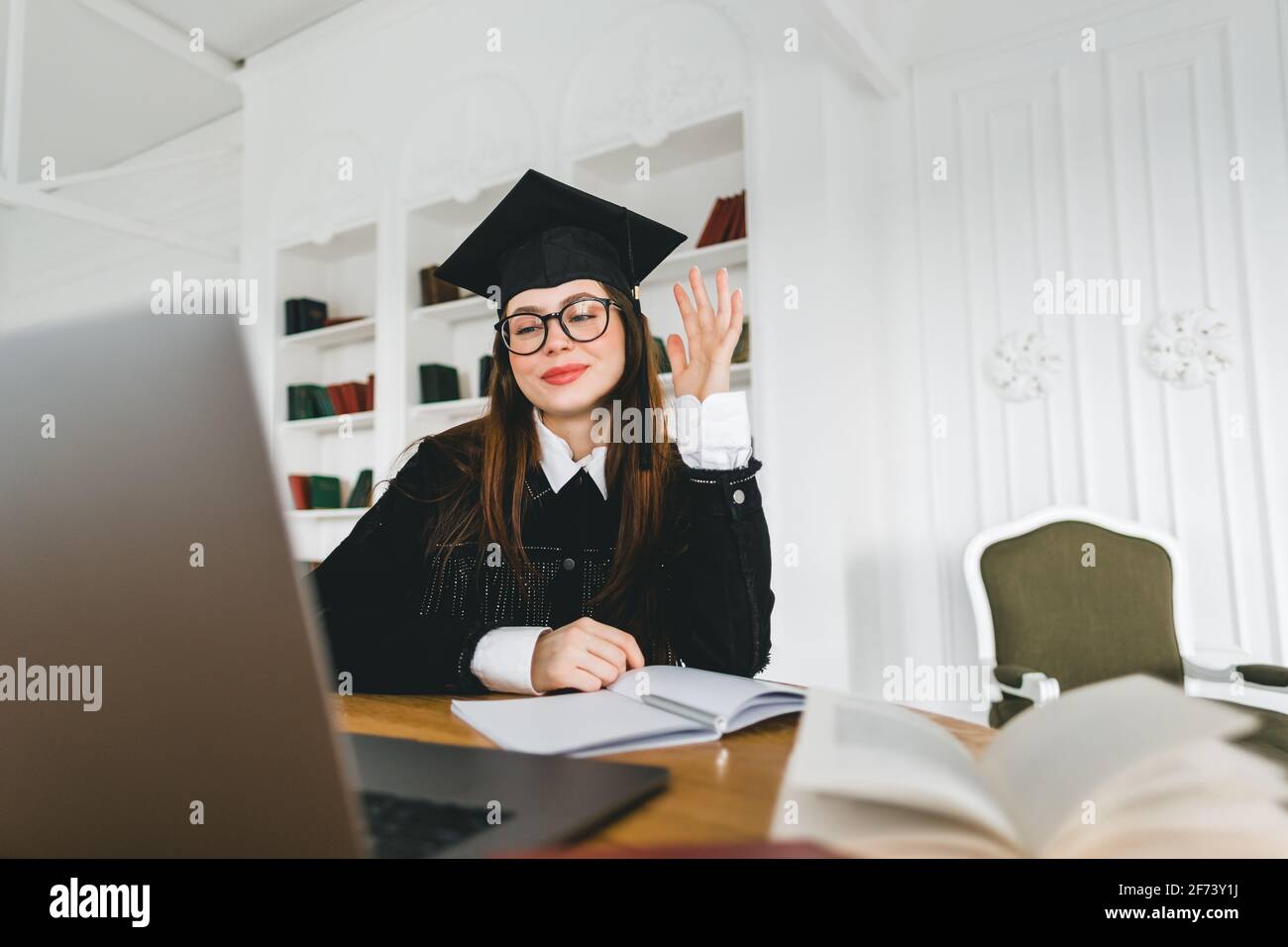 Happy young caucasian woman celebrating college graduation during a video call with friend or family. Online graduation ceremony concept Stock Photo