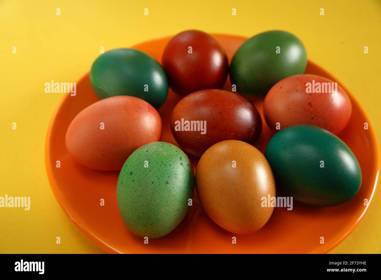 Colorful painted easter eggs on orange plate close up yellow background, symbool of spring Stock Photo