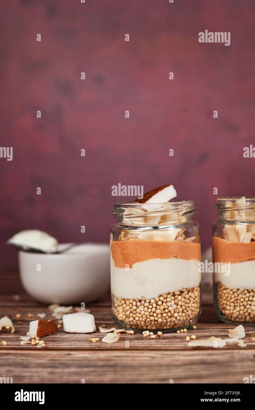 Healthy layered breakfast or dessert with puffed quinoa grains, yogurt and coconut flakes and pieces in glass Stock Photo