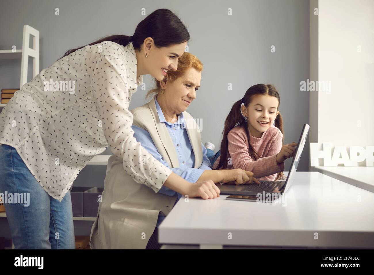 Adult daughter grandchild teaching elderly grandmother to use internet on laptop Stock Photo