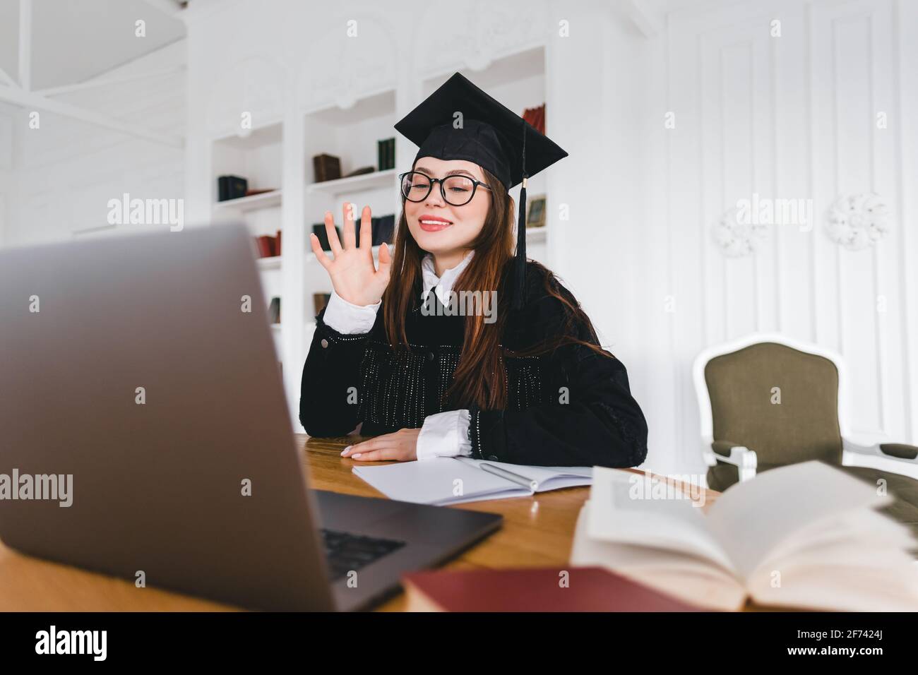 Happy young caucasian woman celebrating college graduation during a video call with friend or family. Online graduation ceremony concept Stock Photo